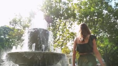 Yazlık takım elbiseli bir kız yazın çeşmenin yanında yürür. Ağır çekim. Moda renkli etek, büyük şapka. Denize karşı güzel bir kız. Kız saçını düzeltiyor. Yaz tatili. Kolay yürüyüş.