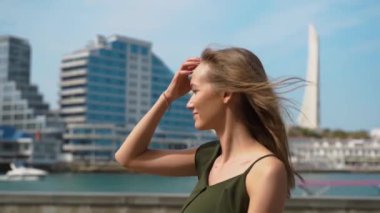 Yazlık takım elbiseli güzel bir kadın deniz kenarında arka planda geziniyor. Denize hayranım. Moda renkli etek. Denize karşı güzel bir kız. Kız saçını düzeltiyor.