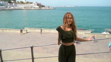 Yazlık takım elbiseli güzel bir kadın arka planda deniz kenarında geziniyor. Ağır çekim. Moda renkli etek, büyük şapka. Denize karşı güzel bir kız. Kız.