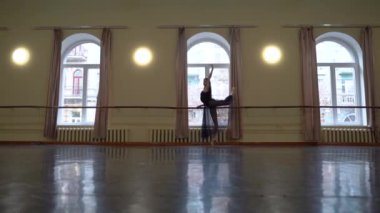 Beyaz etekli baş balerin ve dans sınıfında bale barının yanında bale pozisyonu almak için sivri uçlu esneme hareketleri. Dans stüdyosundaki genç klasik dansçı kadın. Bale sınıfı eğitimi. Bale okulu