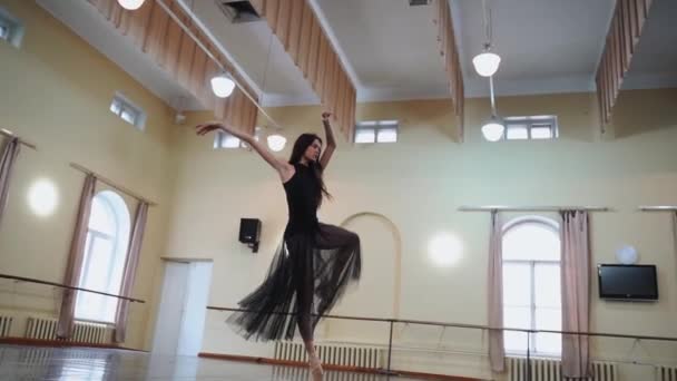 ポントシューズとブラックバレエドレスのプリマバレリーナは美しいダンスの動きを示しています 優雅な動きとプラスチック 大ホールのクラシックバレエの素晴らしいバレリーナダンスの要素 ダンス — ストック動画