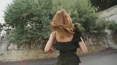 Yaşlı caddede koşuşturan genç yetişkin kadın turistin arka görüntüsü, saçlar çok güzel gelişiyor. Saçlar yana. Park arka planında koşan sevimli, güzel bir kız yolcunun arka manzarası. Kasaba yaşam tarzları