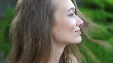 Yakın plan. Park alanının önündeki çekici bir kadının portresi. Gülümseyen kız. Rüzgar saçlarını dalgalandırıyor, yaz kıyafetleri içinde çekici bir kız. Mavi gözler. Denize karşı güzel bir kız. Kız onu düzeltiyor.