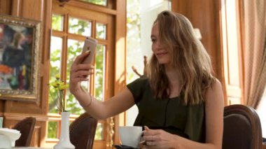 Akıllı telefondan selfie çeken güzel bir kadın. Genç ve güzel bir kadın kafeteryada akıllı telefonuyla selfie çekiyor. Telefondaki selfie, telefondaki fotoğraf, telefondaki resim, telefondaki selfie.