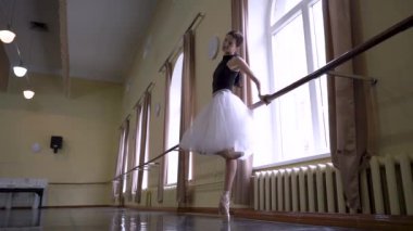 Beyaz etekli genç balerin dans sınıfında bale pozisyonu alıyor. Dans stüdyosundaki genç klasik dansçı kadın. Bale sınıfı eğitimi. Bale okulu konsepti. Yavaş
