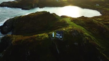 Hava 4k. Baltimore, County Cork 'ta kayalık bir sahil manzarasında pitoresk bir deniz feneri. Sherkin Adası 'ndaki deniz fenerinin üzerinden İrlanda' daki Baltimore Beacon 'a uçun. Bir ev.