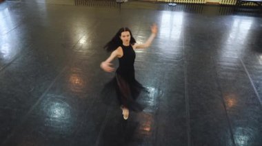 Siyah elbiseli profesyonel balerin büyük bir eğitim salonunda dans ediyor. Siyah zeminde dans et. Opera binasının eğitim salonunda bir balerin dans ediyor. Siyahlı bir balerin tek başına dans eder