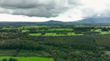 Bu nefes kesici hava çekimi yukarıdaki bulutlu gökyüzünün altındaki canlı tarlaları ve yemyeşil ormanları güzel bir şekilde gösteriyor. Ormanın üzerinden uçmak, doğal arka plan hareketi. Yüksek kalite 4k görüntü