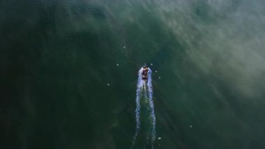 Göz kamaştırıcı bir hava manzarası, berrak bir gökyüzünün altında geniş bir parıldayan su kütlesinin yüzeyinde huzur içinde yüzen bir tekne gösteriyor. Sis dolu arka planda balıkçı teknesi var. Martılar uçuyor