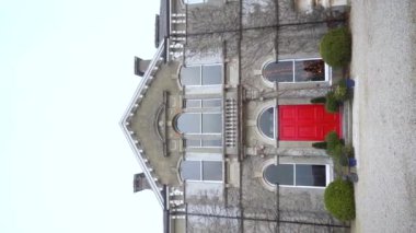 Dikey. Büyüleyici bir video, sarmaşıklarla çevrili canlı kırmızı kapılı görkemli bir taş bina sergiliyor ve çarpıcı mimarisini vurguluyor. Ağır çekim. Yüksek kalite FullHD