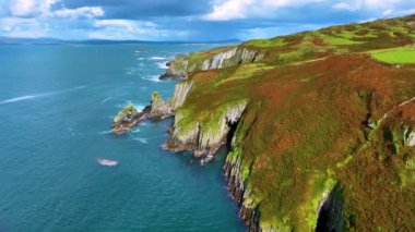 Bu hava görüntüleri, sakin okyanusun çarpıcı bir uçurum manzarasını gösteriyor. Kamera görkemli kayalıkları ve kıyıya vuran nazik dalgaları yakalıyor. Baltimore Co Cork, İrlanda. Yüksek kalite 4k görüntü