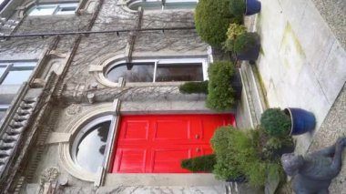 Dikey. Bu video, bir heykelin yanındaki mimari yapının çarpıcı kırmızı kapısının görsel anlatımını inceliyor ve izleyicileri hikayelerini hayal etmeye çağırıyor. Ağır çekim 120 Fp. Yüksek kalite.