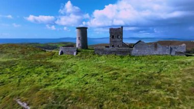 Büyük bir adanın tepesindeki antik deniz feneri kalıntılarının üzerinden uç. Yeşil bir ada ve İrlanda 'nın ortasındaki antik bir kalenin kalıntıları. Deniz manzarası ve yağmur bulutlarına karşı antik kalıntılar