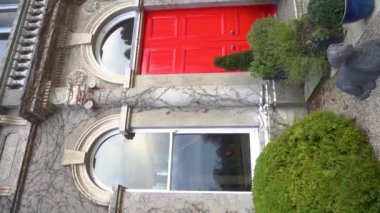 Şaşırtıcı derecede güzel bir kırmızı kapı zarif mimari detaylarla çerçevelenir ve yemyeşil ile çevrilidir. Eski bir kır evinin lüks dış cephesi. İrlanda. Ağır çekim. Yüksek kalite FullHD