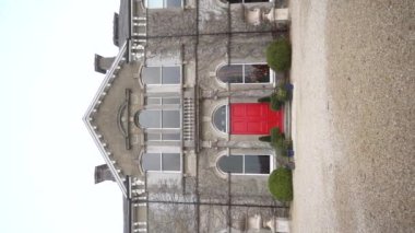 Dikey. Büyüleyici bir video, sarmaşıklarla çevrili canlı kırmızı kapılı görkemli bir taş bina sergiliyor ve çarpıcı mimarisini vurguluyor. Ağır çekim. Yüksek kalite FullHD