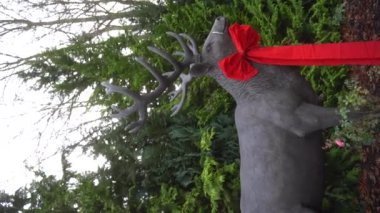Geyik heykeli, boynuzları yeşil köknar ağaçlarının arka planında siyah bir fiyonk ile süslenmiş. Noel için dekoratif ren geyiği süslemesi. Noel sembolü. Mutlu noeller. Yüksek kalite 4k görüntü