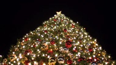 Güzel aydınlatılmış bir Noel ağacı yıldızlarla dolu huzurlu gece gökyüzüne karşı ışıldıyor. Oyuncaklarla süslenmiş yeşil ağaç, hediyeler, hediye kutuları, yanıp sönen çelenkler, yanan lambalar