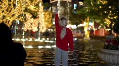 Bir çocuk parıldayan ışıklardan büyülenmiş, parıldayan bir çeşmenin yanında duruyor, masumiyet ve neşe sahnesi yaratıyor. Sıcak Noel atmosferi. Yüksek kalite 4k görüntü