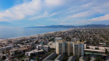 Bu hava manzarası, deniz kenarındaki binalarını ve manzaralı dağlarını aydınlatan canlı bir kıyı şehrini gösteriyor. Venice Kanalı, Marina del Rey, LOS ANGELES, CALIFORNIA, ABD, Ekim 24, 2024. Yüksek