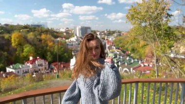 Genç bir kadın, parlak sonbahar renkleriyle dolu canlı ve canlı şehir zeminine karşı sevinçle ayakta duruyor. Sıcak bir kazağa sarılmış neşeli bir kadın, manzaranın tadını çıkarıyor.