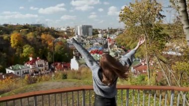 Şehirdeki canlı sonbahar sezonunda güzel manzaralı bir manzarayla neşeyle kutlayan bir kadın. Modern şehir yaşam tarzı ve mutluluk kavramı. Ağır çekim. Yüksek kaliteli HD görüntüler