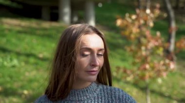 Düşünceli ve üzgün bir kızın portresi rahat bir kazak giyen genç bir kadın huzurlu bir park gününün tadını çıkarıyor, çeşitli düşünceli anlarda görüntüleniyor, doğada huzuru buluyor. Ağır çekim. Yüksek kaliteli HD