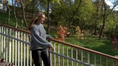 Bu huzurlu videoda, sakin bir parktaki köprüde bulunan genç bir kadın düşünceli bir şekilde gökyüzüne bakarken doğa tarafından çevrelenmiş bir şekilde yansıyor. Modern şehir yaşam tarzı ve mutluluk kavramı. Yavaş