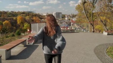 Genç bir kadın, parktaki güneşli bir sonbahar gününün keyfini çıkarmaktan zevk alır. Etrafı canlı sonbahar renkleriyle çevrilidir. Modern şehir yaşam tarzı ve mutluluk kavramı. Ağır çekim. Yüksek kaliteli HD görüntüler