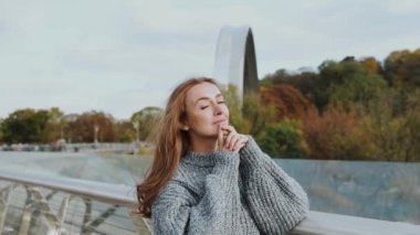 Samimi bir kazak giyen düşünceli bir kadın güzel ve manzaralı bir sonbahar arka planına karşı duruyor, dinginlik saçıyor. Ağır çekim. Yüksek kaliteli HD görüntüler