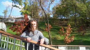 Genç bir kadın renkli yapraklarla dolu canlı bir parktaki güzel sonbahar manzarasının tadını çıkartıyor. Şehir arka planında uzun saçlı, kalın kazaklı bir kızın vesikalığı. Ukrayna