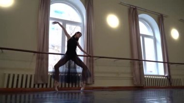 Beyaz etekli baş balerin ve dans sınıfında bale barının yanında bale pozisyonu almak için sivri uçlu esneme hareketleri. Dans stüdyosundaki genç klasik dansçı kadın. Bale sınıfı eğitimi. Bale okulu