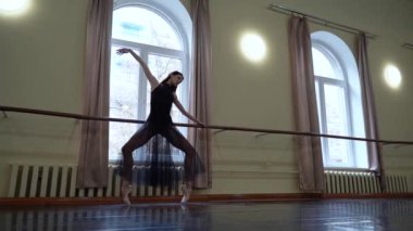 Beyaz etekli baş balerin ve dans sınıfında bale barının yanında bale pozisyonu almak için sivri uçlu esneme hareketleri. Dans stüdyosundaki genç klasik dansçı kadın. Bale sınıfı eğitimi. Bale okulu