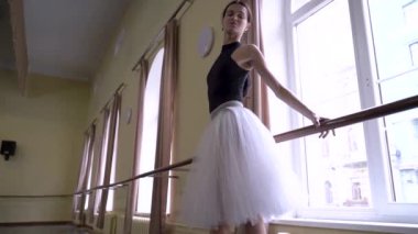 Beyaz etekli genç balerin dans sınıfında bale pozisyonu alıyor. Dans stüdyosundaki genç klasik dansçı kadın. Bale sınıfı eğitimi. Bale okulu konsepti. Yavaş