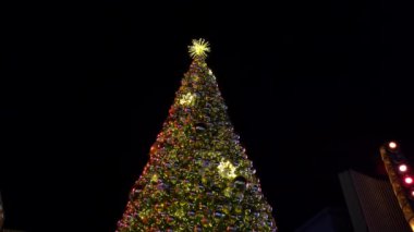 Güzel aydınlatılmış bir Noel ağacı yıldızlarla dolu huzurlu gece gökyüzüne karşı ışıldıyor. Oyuncaklarla süslenmiş yeşil ağaç, hediyeler, hediye kutuları, yanıp sönen çelenkler, yanan lambalar