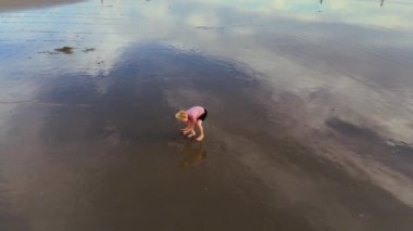 Hava 4k. Genç bir çocuk, güzel, berrak bir gökyüzünün altında ıslak ve yansıtıcı bir plajda neşeyle oynuyor. LOS ANGELES, CALIFORNIA, ABD, 10 Ekim 2024. Ağır çekim. Yüksek kalite