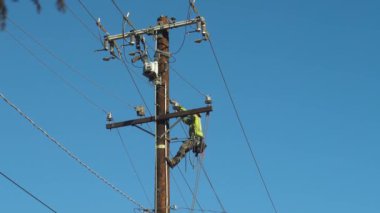 Kendini işine adamış bir kamu işçisi açık mavi gökyüzünün altındaki elektrik hatlarında gerekli bakımı gerçekleştiriyor. Görüntü ekiplerin Pasadena, California 'nın yeniden inşası için özenle çalıştıklarını gösteriyor.