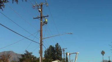 Adanmış bir elektrik işçisi, tüm elektrik hatlarının güvenli ve çalışır durumda olduğundan emin olmak için uzun bir direğe tırmanıyor. Pasadena, California 'da devam eden yeniden inşa çalışmalarının görüntüleri