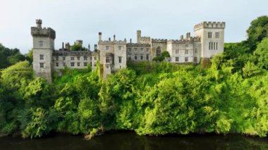 Gün batımında yeşil ağaçlara sarılı, nehrin kıyısında pitoresk bir kale. Akşam güneşi Castle. Waterford Ireland 'ın verimli kırsalındaki Lismore Kalesi ve Knockmealdown Dağları Antik Doğu