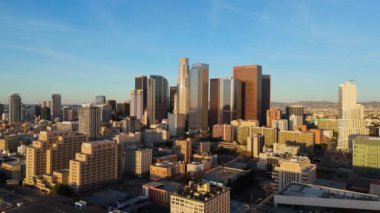 Sıcak güneş ışığıyla aydınlatılan yüksek binaların canlı mimarisini yakalayan, altın saat boyunca şehrin ufuk çizgisinin etkileyici bir hava görüntüsü. Detaylı şehir manzaralarının bir karışımı