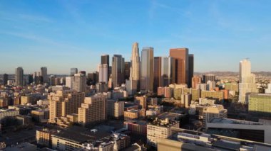 Sıcak güneş ışığıyla aydınlatılan yüksek binaların canlı mimarisini yakalayan, altın saat boyunca şehrin ufuk çizgisinin etkileyici bir hava görüntüsü. Detaylı şehir manzaralarının bir karışımı