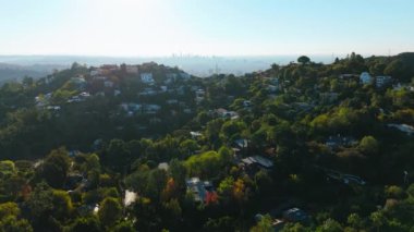 Bu hava görüntülerinde dağlar ve yeşillikler arasında pitoresk bir şehir gösteriliyor, şehir yaşamını doğayla harmanlıyor, tepelerdeki büyüleyici evleri gözler önüne seriyor. Los Angeles, Kaliforniya, ABD, 2024. Yüksek kalite 4k