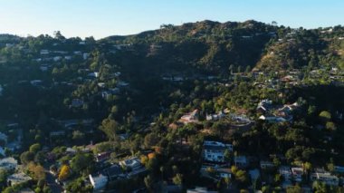 Hollywood Hills, Los Angeles, California 'da ilerleyen bir hava aracı. Lüks yamaçlardaki evleri, yemyeşil alanları ve nefes kesici panoramik manzaraları gösteriyor. Bu görüntü