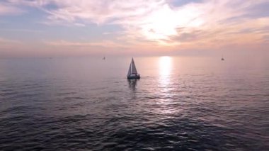 Günbatımında Kaliforniya kıyısı yakınlarında Pasifik Okyanusu 'nun sakin sularında süzülen bir yelkenlinin sakin hava görüntüsü. Batan güneşin altın rengi deniz yüzeyine yansıyor.