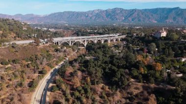 5 Ocak 2025 'te Pasadena, Kaliforniya' daki Colorado Köprüsü 'nün nefes kesici hava görüntüsü. İkonik köprü görkemli San Gabriel Dağları ile yemyeşil üzerine uzanır.