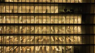 Camdan bir gökdelenin ofis pencerelerinden sinematik bir görüntü. İş adamları geç saatlere kadar çalışıyor. Bir gökdelenin penceresinin yakınındaki bir dronun panoraması. Yüksek kalite 4k