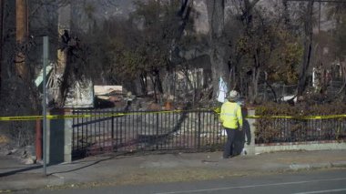 15 Ocak 2025 'te Pasadena, Kaliforniya' da yanmış bir mülkü güvenlik yeleği giymiş bir müfettişi incelerken gösteren statik görüntüler. Sahne, kömürleşmiş ağaçlarla çıkan bir yangının sonrasını vurguluyor.