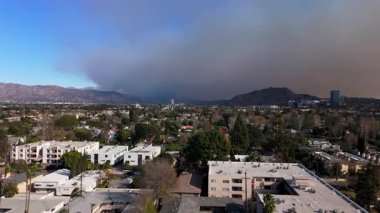 Dramatik bir hava görüntüsü, yakındaki bir yangından kaygı verici bir şekilde yükselen dumanla geniş bir şehir manzarası sunuyor. Dramatik bir hava görüntüsü geniş bir şehir manzarasını kaygı verici bir şekilde dumanla sunar.