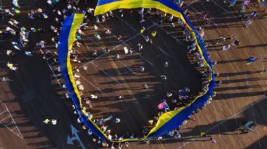 Büyük bir Ukrayna bayrağının yukarıdan görünüşü Santa Monica İskelesi, Los Angeles, Kaliforniya 'da neredeyse tam bir daire oluşturuyor. İnsanlar bayrağın etrafını sarıp tahta kaldırıma uzun gölgeler düşürüyor.