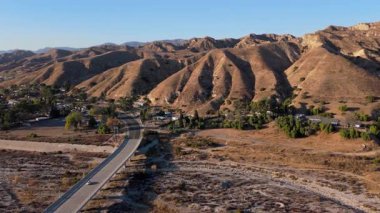 Los Angeles California 'daki engebeli dağların arasından geçen dolambaçlı bir yolda iniş yapan bir hava aracı görüntüsü. Kuru arazi dağınık yeşillik ve konut evleriyle çelişiyor.