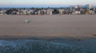10 Ekim 2024 'te Los Angeles, Kaliforniya' daki Venice Beach 'in hava görüntüleri. Kamera sağdan sola hareket ediyor, kumlu kıyı şeridini, okyanus dalgalarını, bir cankurtaran kulesini ve sahil kenarını yakalıyor.
